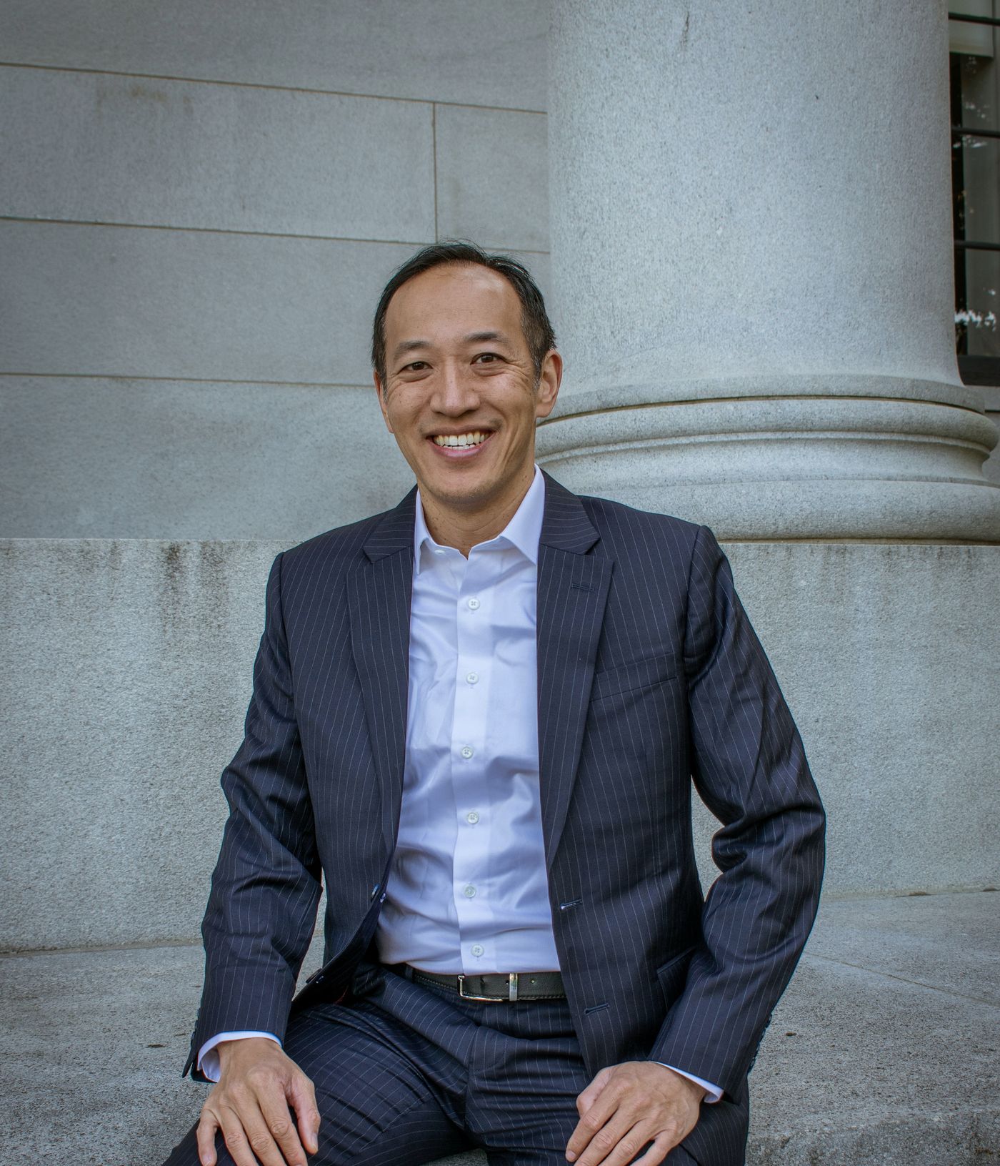 Nikky Kho seated among stone columns in a navy suit
